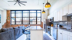 A modern kitchen with a large island, white cabinets, and a brick accent wall. - Downtown Loft w/Parking, Fitness & Movie room (Knoxvile)