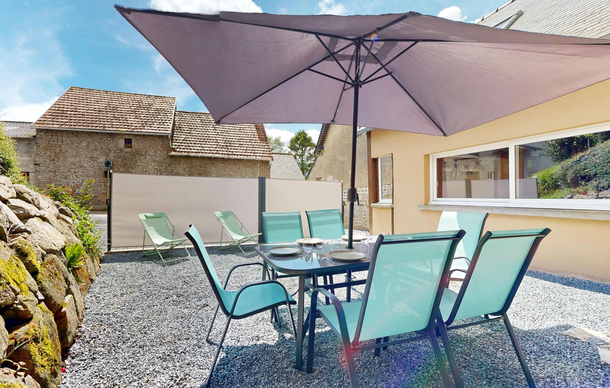 Une terrasse extérieure avec une table et des chaises, un grand parasol et un mur en pierre.