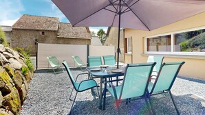 Un patio al aire libre con una mesa, sillas, un paraguas grande y una pared de piedra.