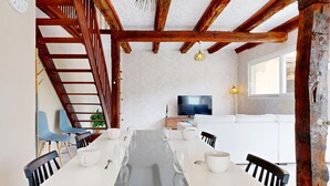 Un comedor con una mesa larga, sillas y un televisor al fondo.