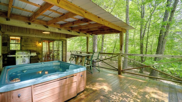 Eine Holzterrasse mit Whirlpool, Grill, Tisch und Stühlen.