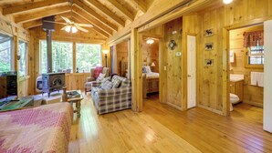 Ein Holzblockhaus-Interieur mit einem Bett, einer Karo-Couch, einem Kamin und einem Badezimmer.