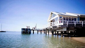 A pier extending into calm water with a building featuring balconies and a covered walkway.