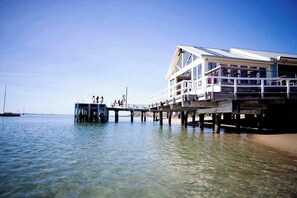 A pier extending into calm water with a building featuring balconies and a covered walkway. - Park Cottage Barwon Heads With Fire, Pet friendly (Barwon Heads)