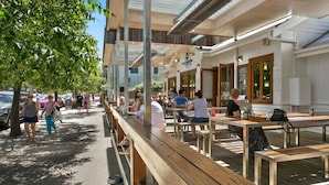 An outdoor seating area with wooden benches and tables, a covered walkway, and a building with a sign.