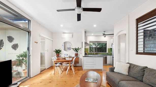 A modern living room with a flat-screen TV, a wooden dining table, a sofa, and a ceiling fan.