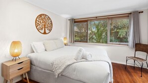 A bedroom with a bed, nightstand, lamp, chair, and window with blinds.