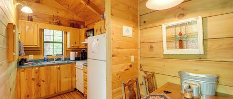 A wooden cabin kitchen with wooden cabinets, a refrigerator, a dining table with chairs, and a hanging light fixture.
