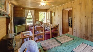 A cozy cabin interior with a wooden ceiling, a ceiling fan, a television on a green cabinet, a leather sofa, and a dining table with placemats. - Hot Tub Haven! Blue Ridge Mountain Gem on 92 Acres (Marion)