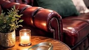 A leather sofa with green cushions, a glass table with a candle, and a potted plant. - Cambridge Garden Studio                  Private Entrance & Free Parking (Cambridge)