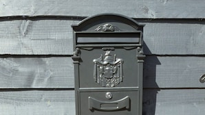 A mailbox with a crest emblem, mounted on a wooden wall with horizontal planks. - Cambridge Garden Studio                  Private Entrance & Free Parking (Cambridge)