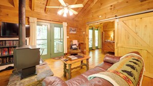 Ein gemütliches Blockhaus mit Kamin aus Stein, Ledersofa, Holzwänden und einem Fernseher.