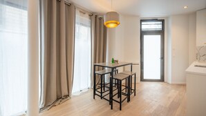 Une pièce moderne comprenant une table à manger et des chaises, un luminaire suspendu et une vue sur l’extérieur par une porte.