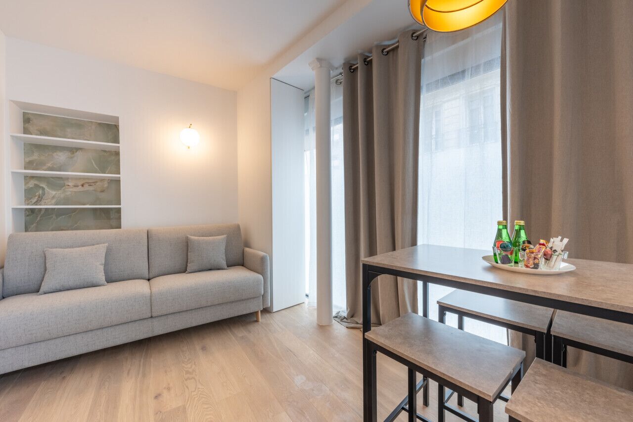 Una sala moderna con un sofá gris, una mesa de comedor con bancos y un mueble de pared.