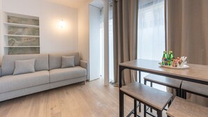 Un salon moderne avec un canapé gris, une table à manger avec des bancs et une étagère murale.