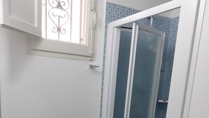 Un baño con bidé, cabina de ducha de vidrio y paredes con azulejos azules.