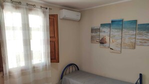 Una habitación pequeña y limpia con una cama, una ventana con cortinas, aire acondicionado y tres obras de arte decoradas con motivos playeros.