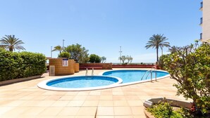 A rooftop pool area with two swimming pools, surrounded by palm trees and a clear blue sky.