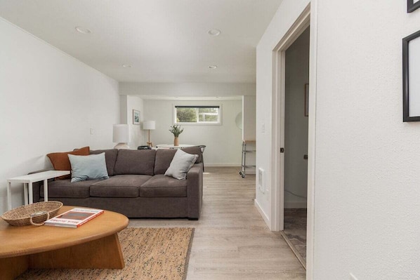Ein modernes Wohnzimmer mit einem grauen Sofa, einem Holztisch und einem weißen Beistelltisch.