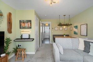Ein Wohnzimmer mit grauem Sofa, einem Holztisch, einer Tastatur und einer Pflanze.