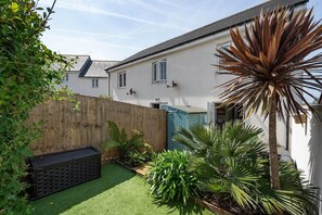 Propiedad residencial con jardín trasero cercado, césped artificial y diversas plantas.