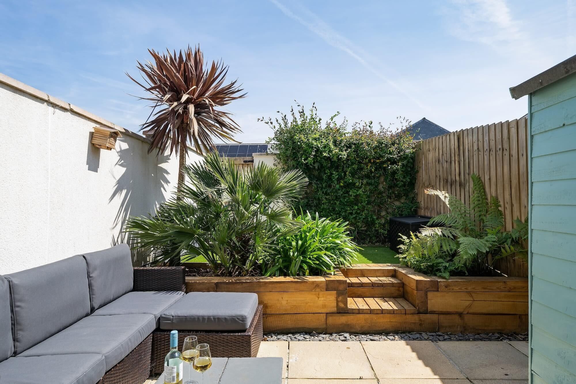 A patio with a grey sofa, a wooden planter, and a variety of plants.