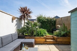 Eine Terrasse mit einer grauen Couch, einem Holz-Pflanzgefäß und verschiedenen Pflanzen.