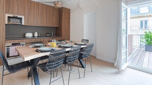 A modern kitchen with wooden cabinets, a built-in oven, and a dining area with a wooden table and black chairs. - Large terrace, air conditioning, 3 bedrooms, Marais (Paris)