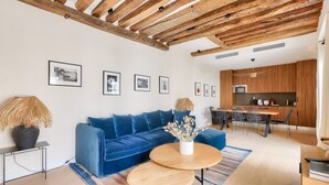 A modern living room with a blue sofa, wooden coffee table, and a dining area with a wooden table and chairs. - Large terrace, air conditioning, 3 bedrooms, Marais (Paris)
