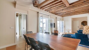 A spacious dining area with a large wooden table and black chairs, a blue sofa, and a ceiling with exposed wooden beams. - Large terrace, air conditioning, 3 bedrooms, Marais (Paris)