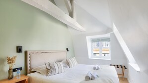 A bedroom with a bed, a bedside table with a vase and a bottle, a window, and a skylight.
