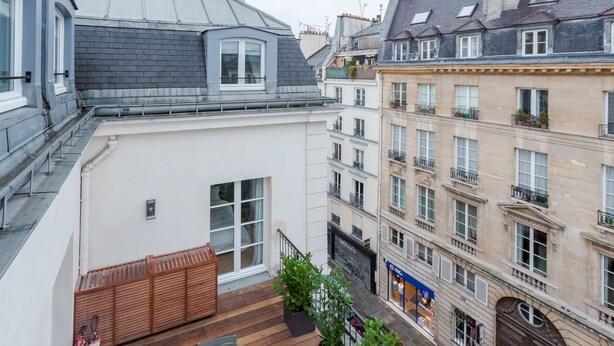 A multi-story building with a balcony, a wooden fence, and potted plants. - Charming Apartment with Air Conditioning - Marais (Paris)