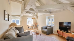 A living room with a sofa, armchair, TV, and a dining area with chairs and a table. - Charming Apartment with Air Conditioning - Marais (Paris)