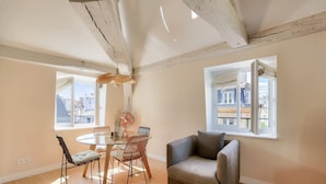 A room with a dining table, chairs, a sofa, and a large window. - Charming Apartment with Air Conditioning - Marais (Paris)