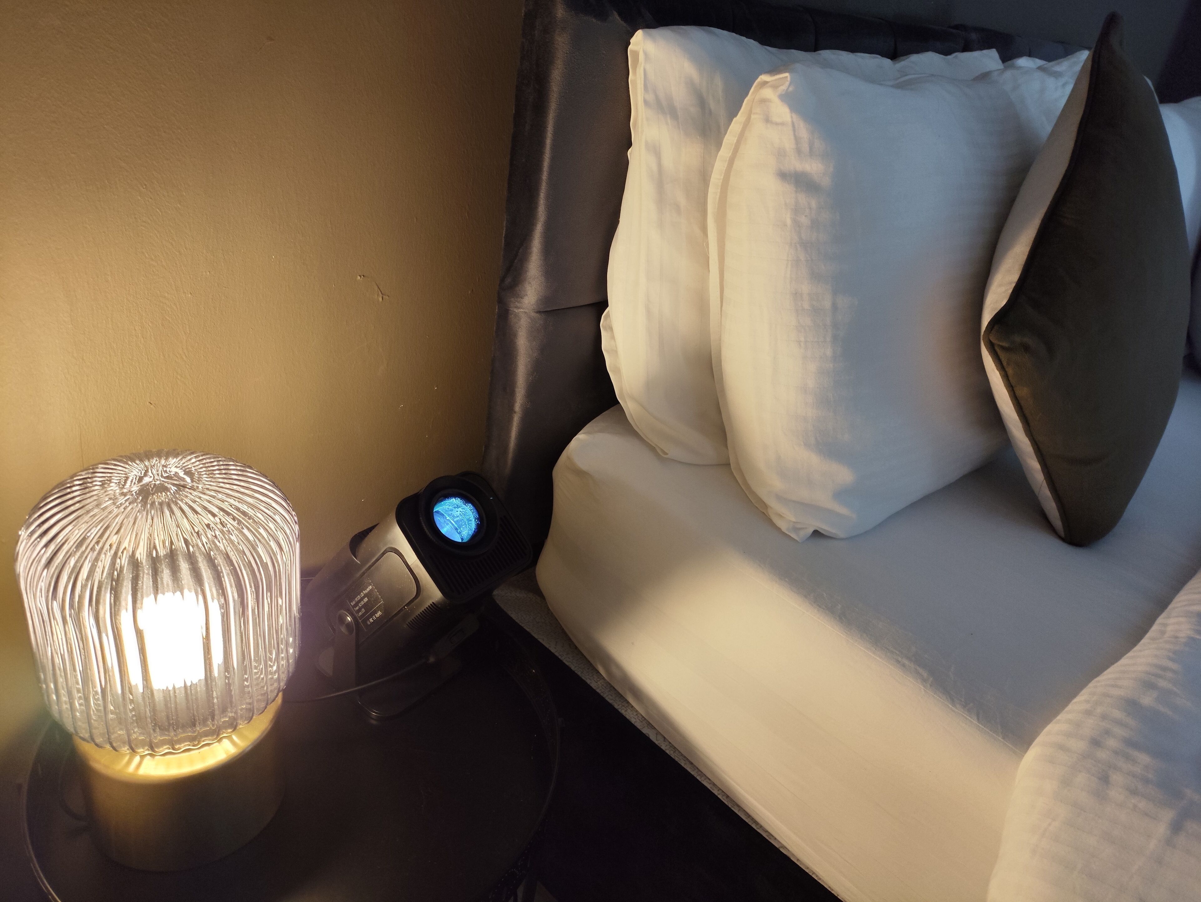 A bed with white pillows and a bedside table with a lamp and a digital clock.