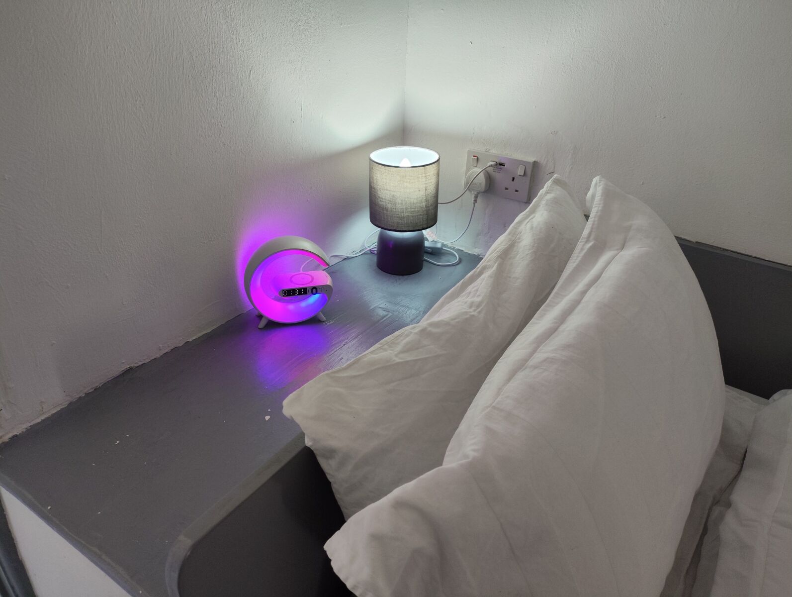 Una mesita de noche con una lámpara y un reloj digital.