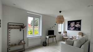 En moderne stue med sofa, fjernsyn, et vindue med udsigt til grønne områder, en radiator og en vægmonteret lampe.