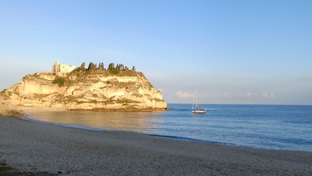 A beach with a rocky cliff and a building on top. - Residenza Stefanelli (Torre Marino, Capo Vaticano)