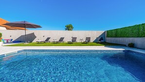 A swimming pool with a clear blue water surface, surrounded by a concrete deck. There are several lounge chairs aligned along the poolside, and a large umbrella providing shade. - Stunning apartment in Tinj (Tinj)