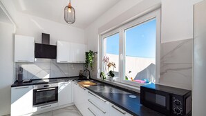 A modern kitchen with white cabinets, a black countertop, and a window providing a view of the outside. - Stunning apartment in Tinj (Tinj)