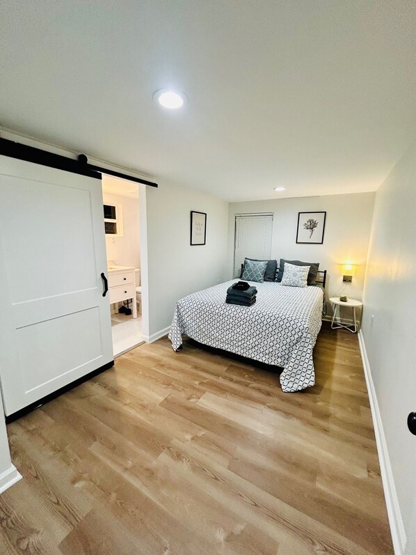 A bedroom with a bed, a bedside table, a nightstand, a door, and a small window.