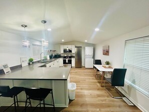 A modern kitchen with white cabinets, stainless steel appliances, a central island with bar stools, and a dining area with a table and chairs.