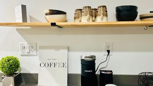 Keittiön työtasolla on Keurig-kahvinkeitin, kahvikapselihylly, valkoinen kahvikuppi, pieni ruukkukasvi ja kyltti, jossa lukee: ”Tämä keittiö on tarkoitettu tanssimiseen.”