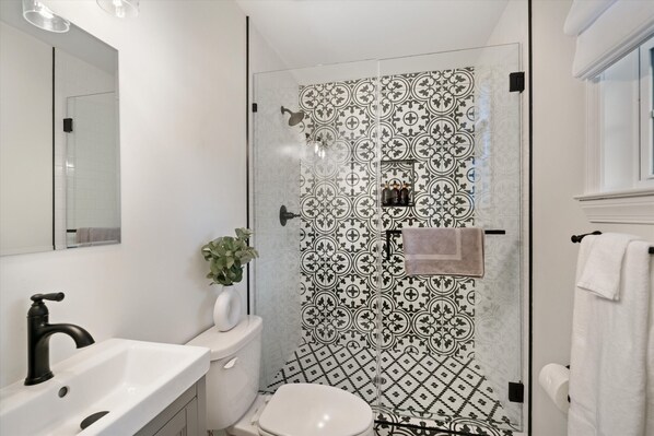 A modern bathroom with a white sink, black faucet, and a glass-enclosed shower with patterned tiles.