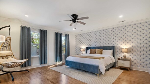 Quarto com cama, cadeira suspensa, ventilador de teto e mesa de cabeceira com luminária.