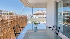 Een balkon met een glazen tafel, twee stoelen en een bloempot.