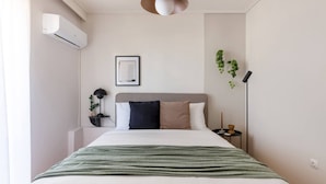 Een keurig opgemaakte slaapkamer met een bed, nachtkastje, lamp en een potplant.