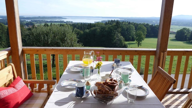 Una mesa colocada en una terraza de madera con una vista panorámica de un lago y un bosque.
