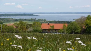 Une maison de campagne avec un toit rouge, entourée de champs et d’un lac.