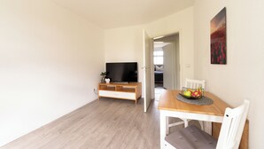 Ein gemütlicher Wohnbereich mit Esstisch aus Holz, einem Fernseher auf einem niedrigen Holzschrank und einem Bild an der Wand.
